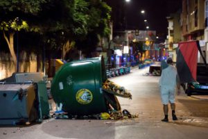 Un hombre porta una bandera junto a unos contenedores volcados en la barriada de Huelin de Málaga. / Foto: Daniel Pérez.